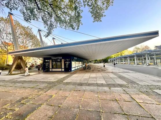 Blick auf den Omnisbusbahnhof. Betonstelen, die an Giraffen erinnern, halten an langen Stahlseilen ein flaches, weißes Betondach