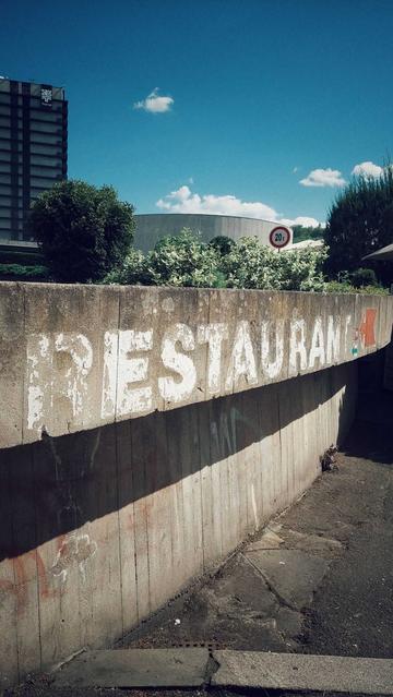 A concrete wall in high noon sun,  with a writing reading "Restaurant". Slightly decayed.