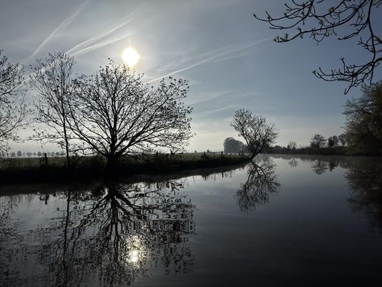 Die Sonne vertreibt den letzten Nebel und spiegelt sich in dem ruhigem Wasser des Entwässerungskanals.