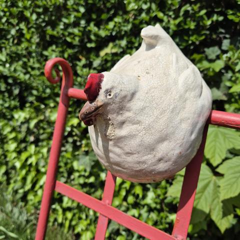 Ein getöpfertes Huhn sitzt auf der Lehne einer metallenen Gartenbank.