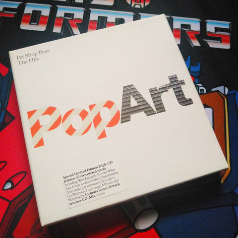 Front of the box for the Pet Shop Boys CD "PopArt: The Hits", a white box with the title presented in bright red and grey. A sticker in the bottom left notes that this is the "Special Limited Edition Triple CD" version.