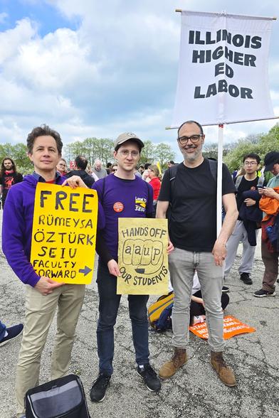Three men at an outdoor protest holding signs that say:
1. Free Rumeysa Ozturk, S.E.I.U. Faculty Forward
2. Hands off our students. A.A.U.P.
3. Illinois Higher Ed Labor