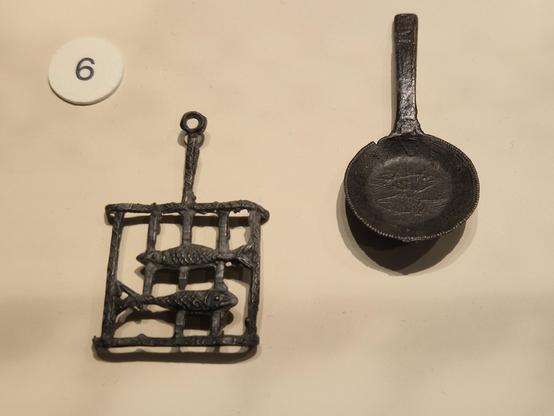 Close up of two Medieval miniatures, perhaps toys, made of tin, of a rack and a frying pan with two fish on and in them. Exhibition at the Rijksmuseum van Oudheden Leiden.