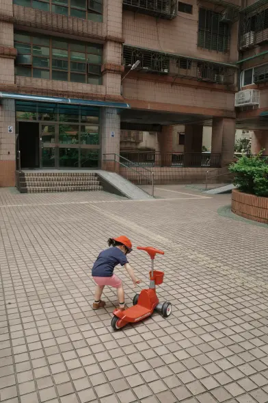 A toddler plays with a scooter in the courtyard of a residential building