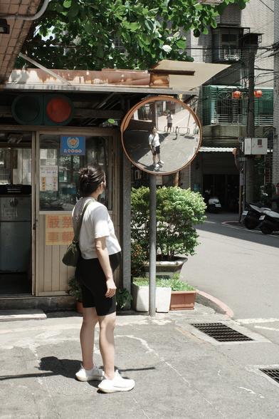 A pregnant woman in an urban setting, with her, the photographer, and their daughter reflected in a traffic mirror in the scene