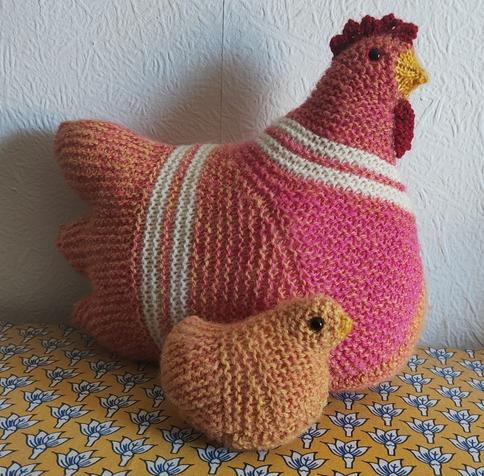 A larger knitted chicken, mostly pink and orange, with a small orange chick by her side, seen sideways on.