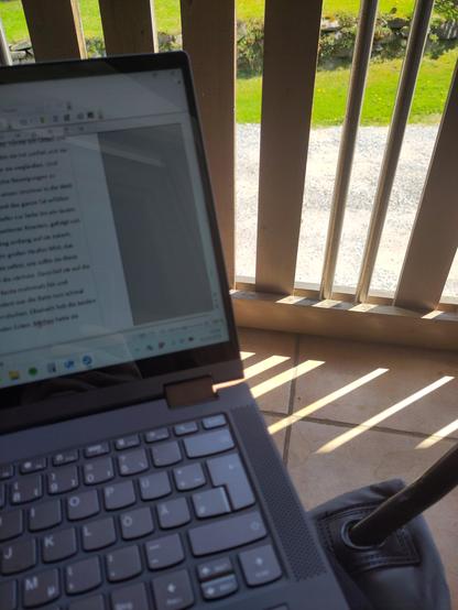 Notebook, im Hintergrund Balkongeländer erkennbar. Sonniger Tag