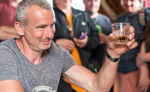 Un homme tenant un verre de whisky avec un orteil conservé dedans, participant à la tradition du cocktail au Sour Toe du Yukon, au Canada.