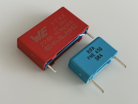 a large red Würth Electronics X2 capacitor and a smaller, blue RIFA capacitor.