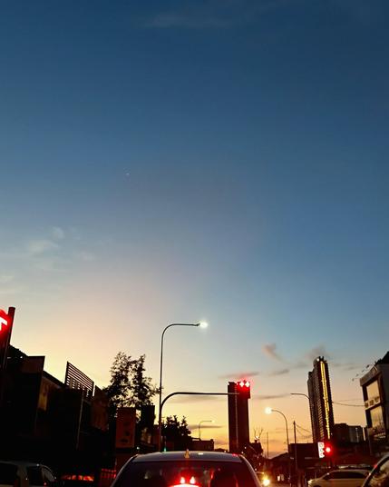 the sun is barely up and yet, it paints the cloudless sky blue, pushing the dark up and away. Meanwhile traffic remains a standstill at a red light