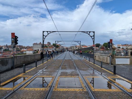 Double rail tracks disappearing into the distance, wet cobblestones in road with puddles reflecting power lines and poles.