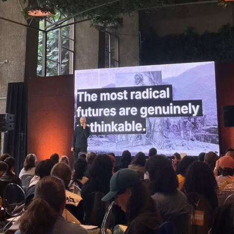 Simon Höher on stage with a slide that reads: "The most radical futures are genuinely unthinkable"