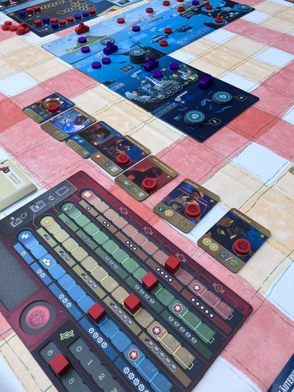 Das Foto zeigt einen Tisch auf dem ein Teil des Aufbaus des Brettspiels „Endeavor - Die Tiefsee“ zu sehen ist. Am unteren Bildrand liegt das Spielertableau, auf dem verschiedene Marker in verschiedenen Leisten bewegt werden. Darüber liegen kleine Spielkarten, welche die verschiedenen Crewmitglieder zeigen: Ökotoxikologin, Steuermann, Start-Crewmitglied, Unterwasser-Fotografin, Schiffstechnikerin, Aquakultur-Forscher. 
Am oberen Bildrand sind fünf große Karten zu sehen, welche die verschiedenen Tiefen des Meeres darstellen. Die oberste in einem hellen Blau bis runter zu fast gänzlich schwarz zur Symbolisierung der Tiefsee.