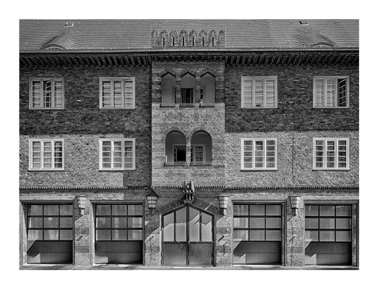 Teilfrontansicht der Feuerwache Berlin Spandau-Nord aus Backstein von 1926.
 Im unteren Teil vier Garagentore in rechteckiger Form, mittig ein Tor mit 2 Torflügeln in teils Trapezform. Darüber 2 Etagen mit je 4 Fenstern mit Butzenscheiben, mittig zwei vorstehende Balkone. Auf dem Dach zwei kleine Walmdachfenster, darüber je eine Dachlucke.