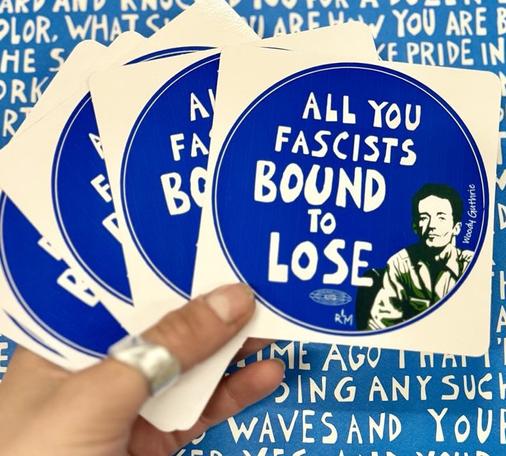 Blue and white image. Blue background with white text. In the center a hand holds four stickers. Stickers are square with a blue circle in the center. Inside of this circle, a portrait of Woodie Guthrie and white text. Text reads "all you fascists bound to lose".