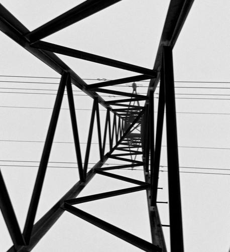 Black and white image, looking up inside a tall high-voltage power column. Parallel wires stretch across at the top from left to right.