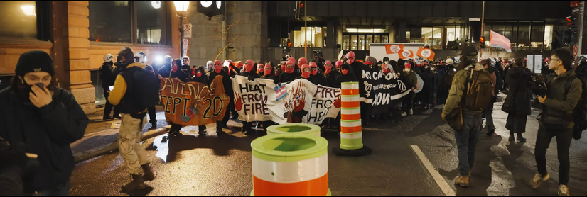 a protest march of people in black wearing pink balaclavas while police try to film faces, the slogan heat from fire, fire from heat is carried at the front
