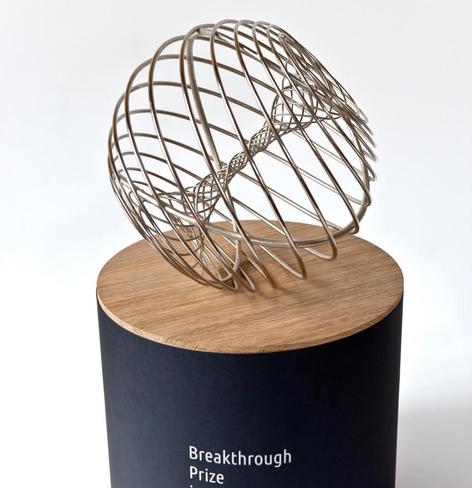 Image of the prize trophy, a metal toroid on a wooden base.