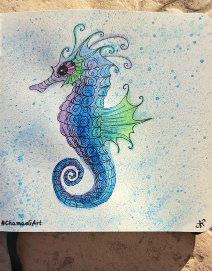 Im kleinen quadratischen Skizzenbuch mit schwarzem Pigmentliner und Aquarellbuntstiften gezeichnet: Ein Seepferdchen mit Doodle-Muster, in Blau, Violett und Grün coloriert. Ein paar blaue und grüne Farbkleckse drumherum.
