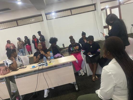 Photo of a group of black women gathering in a conference room in Lusaka, Zambia. There is a group of people standing in the back, as well as several sitting in front of tables, as well as and on the side.  The picture was shot while onboarding with Delta Chat Android took place, and people in the picture consented to publishing.