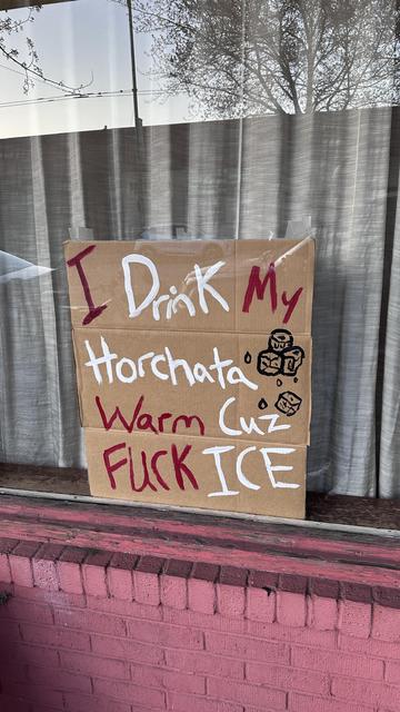 A sign in a window on cardboard that reads: I drink my horchata warm ‘cuz fuck ICE.
