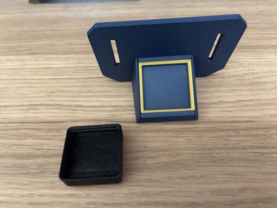 The 3D printed Gridfinity holder has slots to hang from an IKEA SKÅDIS pegboard.  It is blue with a gold highlight around the bin edges.  It is made of multiple pieces slid together.  A 1x1 Gridfinity bin is sitting next to it.