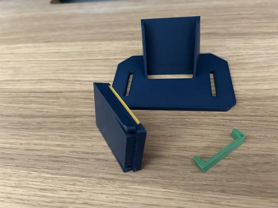 Thre three pieces of the holder.  The biggest part is a single color (blue).  It has a base plate that goes against the pegboard and a support that holds up a tray.  The tray slot goes all the way through.  The tray is two colors (blue and gold).  It has springy tabs that engage divots in the big part.  The third part is a U-shaped clip.