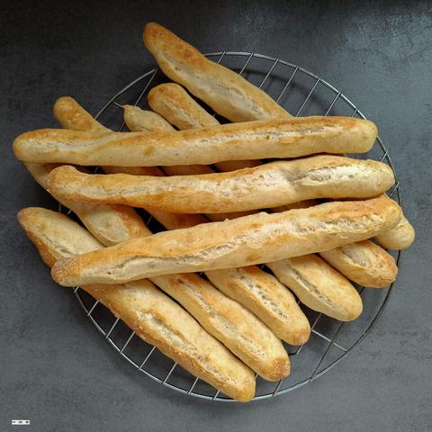 Neun frischgebackene kleine Baguettes liegen auf einem Abkühlgitter.