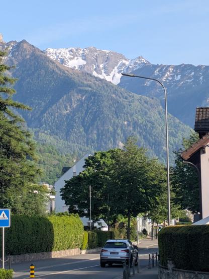 A snow tipped peak rising up from the valley, greenery in front, lining the road
