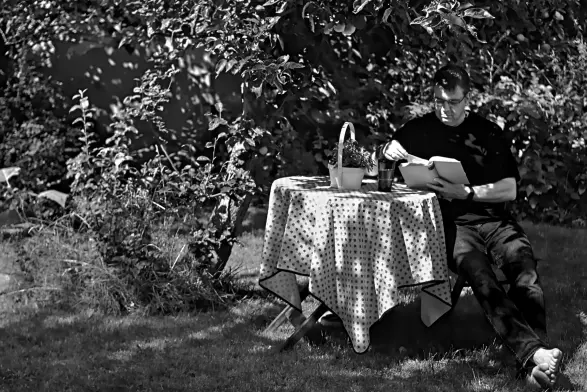 An einem kleinen runden Tisch mit Tischdecke, Blumendeko und einem Kaltgetränk sitzt ein Mann im Schatten eines Apfelbaumes und liest. 
Die Sonne scheint, das Wetter ist herrlich, und ich genieße meinen Platz im Garten.