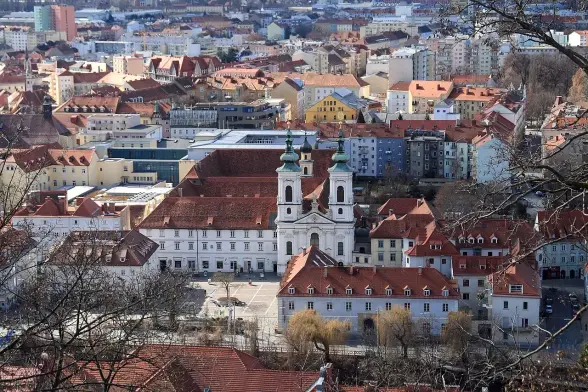 The image appears to show a scenic view of a cityscape featuring buildings with various styles and colors. In the foreground, there is a prominent church or cathedral with distinctive twin towers. The surrounding area includes a mix of residential and commercial buildings, many with red rooftops. Overall, it gives a sense of an urban environment with historical architecture.

Image Credits: Wikimedia / Manfred Werner - Tsui / CC BY-SA 3.0
