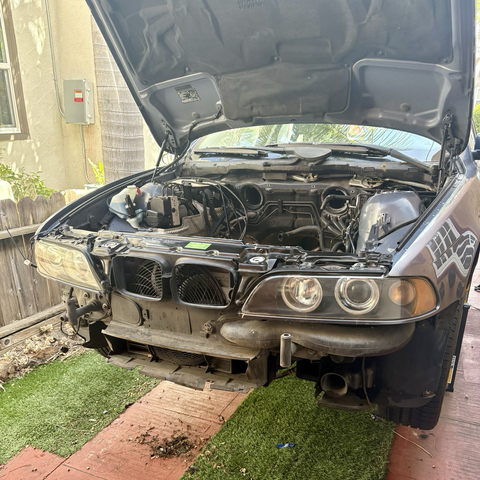 The front end of my blue 2003 BMW 5-series station wagon, lifted up on QuickJacks, with its hood open and its front bumper removed.