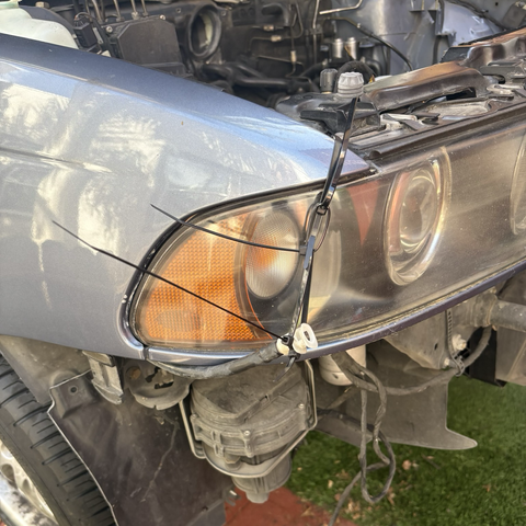 A chain of zip ties run from a headlight mounting tab down the side of the passenger-side headlight to hold up the end of a hose, which connects to the headlight washer hoses in the front bumper, to prevent washer fluid from leaking out.