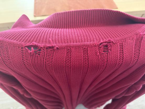 Close up of the area of a long purchased knitted red cardigan which has two holes between the top of the cardigan and the sewn-on collar. One holes is in an area where the stitches were purled, one is in an area where they were knitted, then purled.