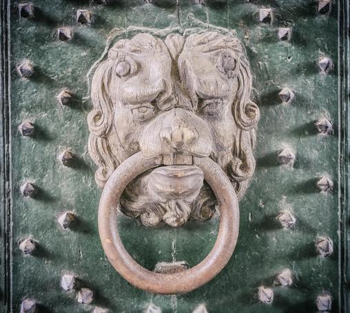 A lion-shaped door knocker on a studded green door.