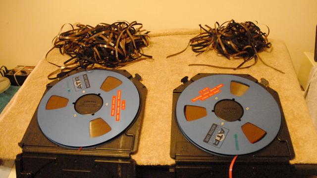 Two reels of 1/4" studio tape containing the stereo mixdown of the album "More Songs About Dragons" by DOUG the Eagle.
These are blue ATR spools with the titles printed on them with old-style Dymo labels.
Above each reel is a tangled mass of tape, containing unwanted sections where the mix was aborted and the gap before the mix restarts has been cut out with razorblades and sticky tape.  Which is how most albums were produced until the 90s.

Keen eyes may note that side 2 has a lot of tape missing - this went into a later remix of the opening track on side 1, and the original version has been spooled onto a 7" tape.