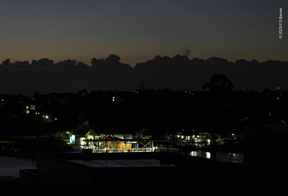 A ferry terminal lit up while nearly all around is dark. A road and lights suggest a hill rising up behind. On the horizon is a line of low cumulus, adding a second skyline. The terminal sign says "Hawthorne".