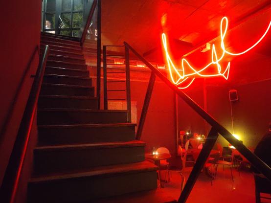 Eine Treppe auf der linken Seite, auf der rechten Seite ein rot ausgeleuchteter Gastraum mit einer Licht Schlange.