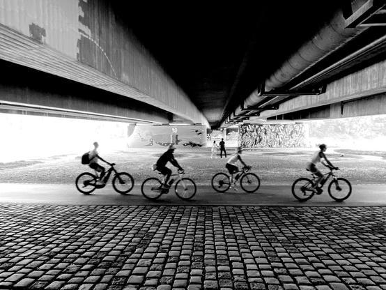 Schwarzweißfoto unter einer Autobahnbrücken mit Fahrradfahrern im Vordergrund; black and white photo unter a big bridge with cyclists in foreground