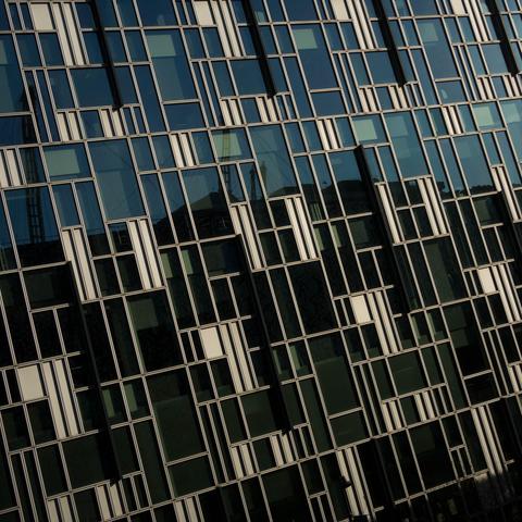 Photo of just a lot of greenish glass across part of the face of a building, separated into rectangles of various sizes by golden-hued metal borders and slim panels, along with the occasional dark protruding slat.