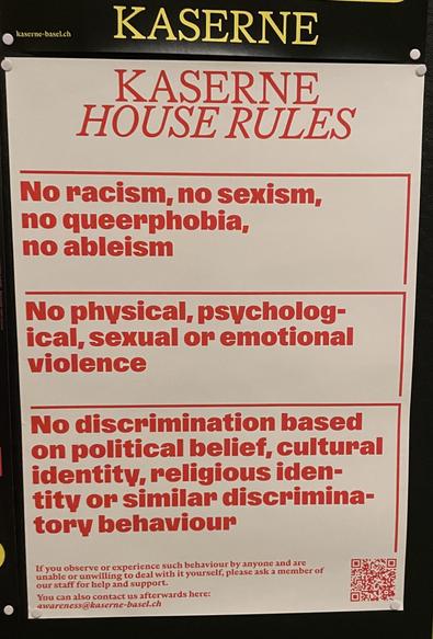 Foto eine weißen Plaketes mit roter Schrift. 
Kaserne 
House Rules 

No racism, no sexism, no queerphobia, no ableism 

No physical, psychological, sexual or emotional violence 

Ni discrimination based on political belief, cultural identity, religious identity or  similar behaviour 

Darunter in kleinerer Schrift: 
If you observe or experience such behaviour by anyone and ar unable or unwilling to dealt with ist yourself, pleas ask a member of our staff for help an Support 
You can also contact us afterwards here: 
awareness@kaserne-basel.ch