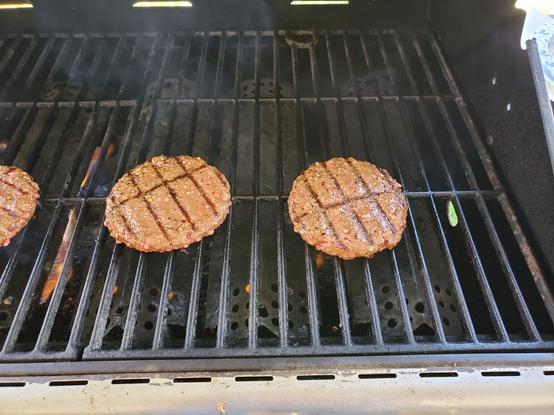 Photo of some burgers on a gas grill.
