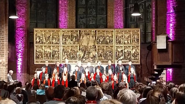 Altar einer Kirche, davor win gemischter Chor in schwarzer Kleidung mit roten Assesioares.