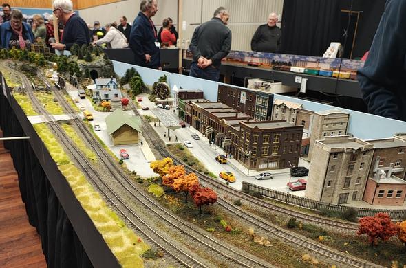 View of a train layout in a hall with people standing around.