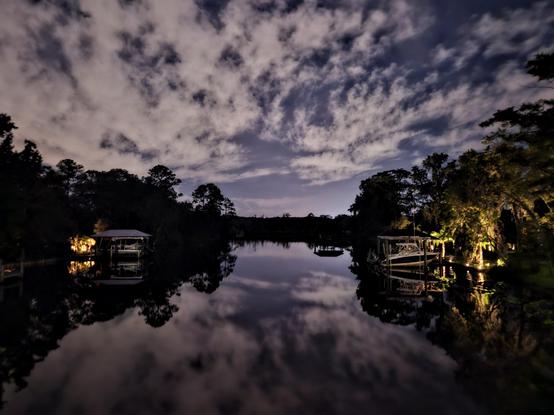 Late night view down a dark waterway winding through tropical foliage,  with illuminated boat docks  on either shoreline glowing like campfires in the night.