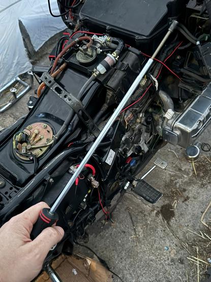 someone holding a very long screwdriver with a spring-loaded tip in front of a slowly-being-reassembled motorcycle.