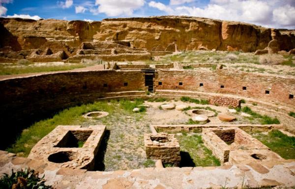 Image of a large, circular, below-ground area surrounded by very finely crafted stone walls. Other ruins are in the background.