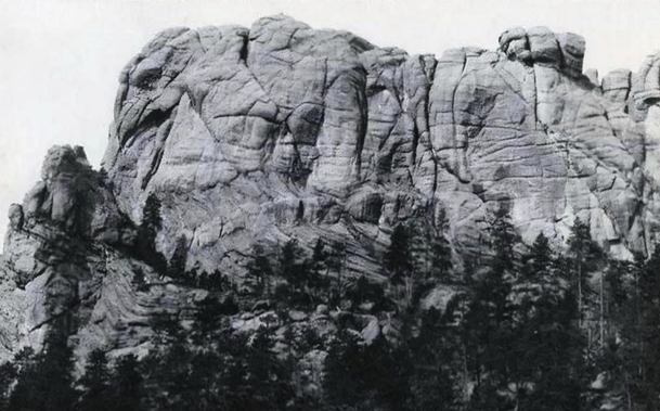 Black and white photo of a large rock outcropping, it's Mount Rushmore before it was carved to show the faces of several US presidents.
