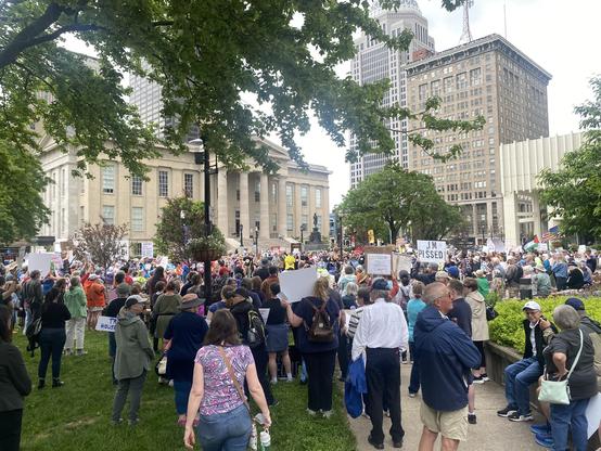 Crowd of protesters gather in park across the street from the courthouse. Man to the right holds up sign: "I'M PISSED!"