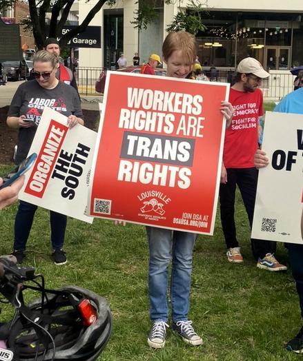 Woman holds large red sign with white letters: "WORKERS RIGHTS ARE TRANS RIGHTS"